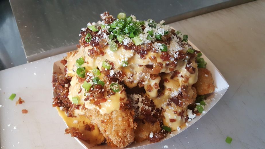 I Don't Know & I Don't Care's Bird Nest is a pair of chicken tenders in cheese sauce with a blend of crumbled bacon, scallions, and cotija cheese on hand-cut potato chips.