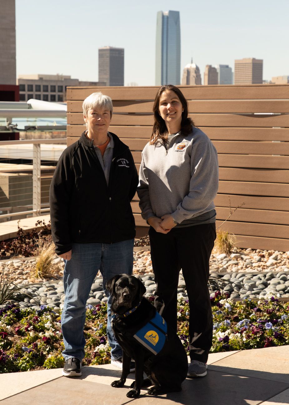 Kristy Doyle, supervisor of therapeutic recreation at the Oklahoma City VA Medical Center, and Sarah Sands, a recreational therapist at the VA, pose with Raisin. Photo by Phillip Ybarra